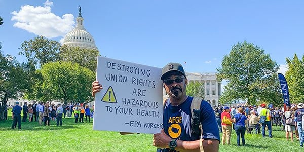 Image of rally goer in front of the US Capitol holding a sign that says "Destroying union rights are hazardous to your health. - EPA worker"