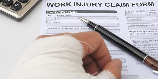 Close up of a person's bandaged hand on top of a Work Injury Claim Form with a pen laying to the side. 