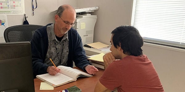 Union steward Bill Mclaughlin and and employee sit at a desk in the Local 2779 office looking at applicable master agreement articles for the issue at hand