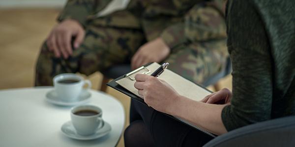 Close-up of psychologist writing down notes while talking to her patient from army