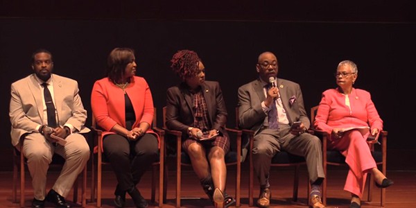 NST Kelley sits on a stage with four other panelists.