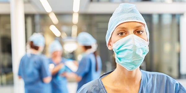 Medical professional wearing scrubs, face mask and hair covering.