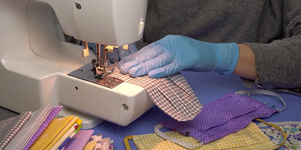 Close up shot of gloved hand making cloth masks at a sewing machine