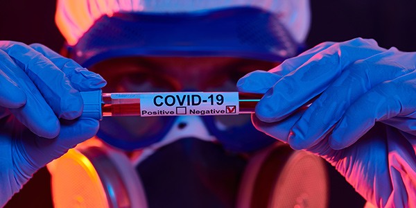 Close up of person wearing protective equipment holding a vile that says COVID-19 with the negative box checked. 