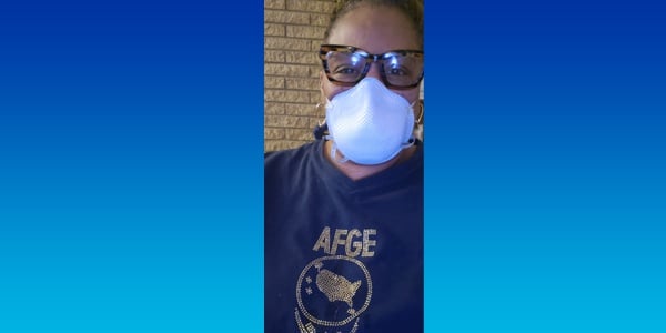 Image of woman with a medical mask covering half of her face. She's wearing a shirt that reads AFGE. 