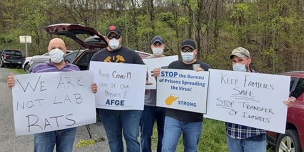 Image of 5 men standing holding signs supporting the halt of the transfer of BOP inmates