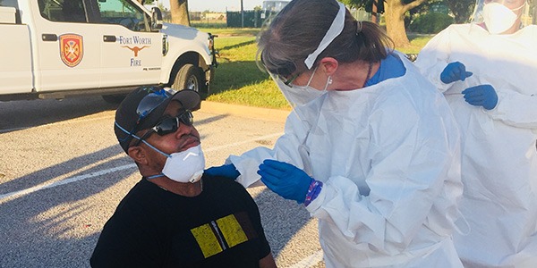 Man seated outside getting a coronavirus test from worker wearing full PPE