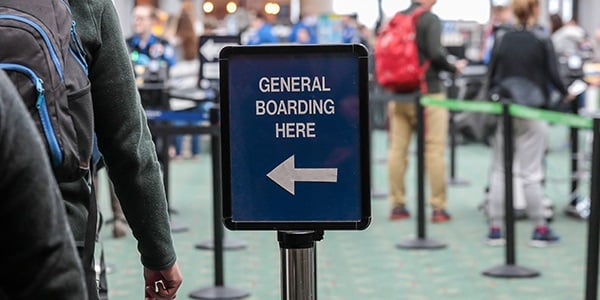 Image of a sign that says General Boarding Here with a left pointing arrow. People are standing in the background.