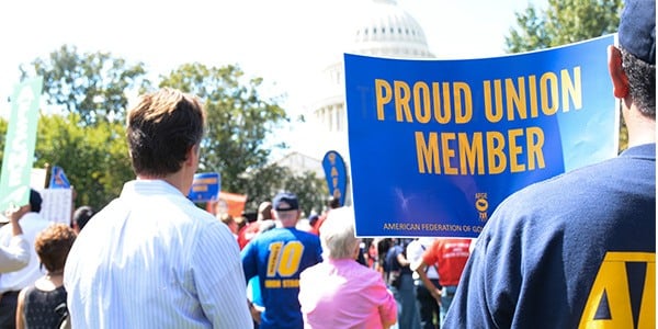 Rally goers outside of US Capitol. One holds a sign that says Proud Union Member