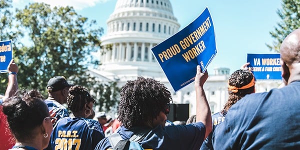 Image of rally goer in front of the US Capitol holding a sign that says Proud Government Worker