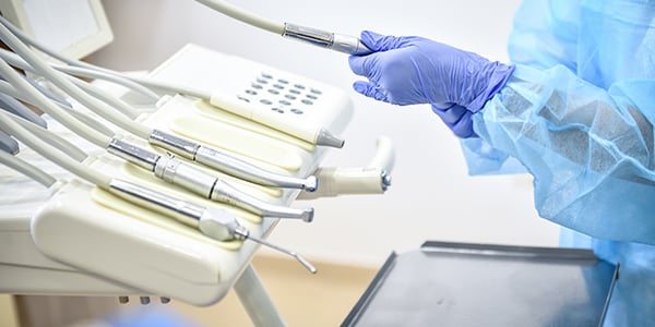 Person in protective equipment and glover standing over dental equipment.