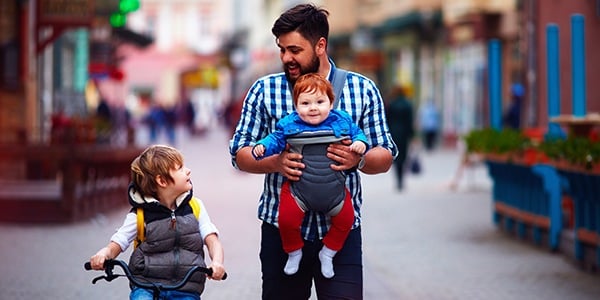 Man walking with two children, one on a bike and one he his holding