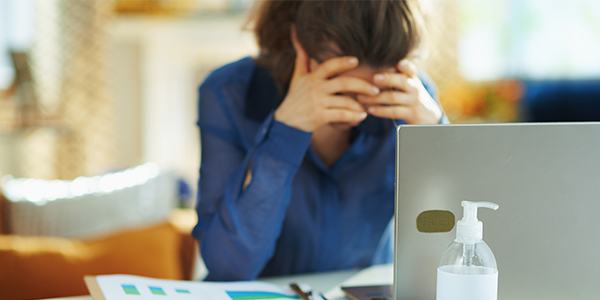 White woman sitting in front of her computer with her head bent in her hands