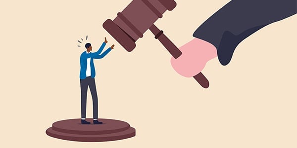 Cartoon of black person standing on a gavel stand with a gavel over their head held by a white hand