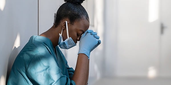 Black woman in scrubs sitting with head in her hands