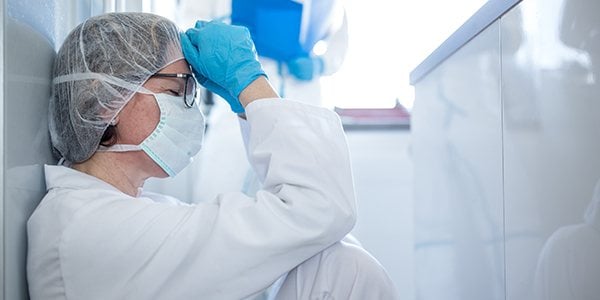 Medical professional in PPE sitting on floor with head in hands