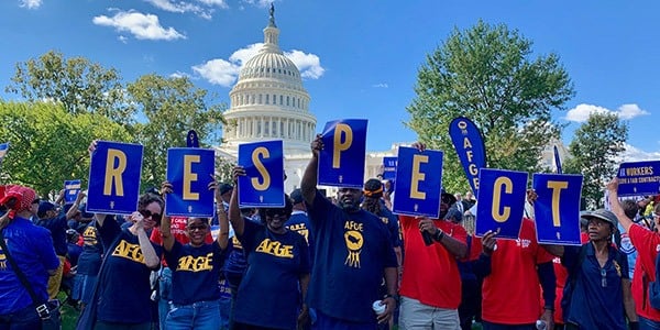 Rally goers holding up signs together in front of the Capitol that read RESPECT.