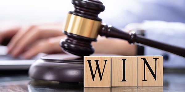 Gavel next to a person's hand. In front of the gavel are the letters WIN