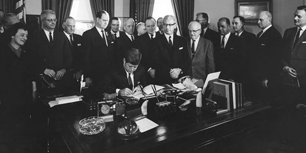 President John F. Kennedy signs Executive Order for the Task Force on Employee-Management Relations in the Federal Service surrounded by government and labor officials