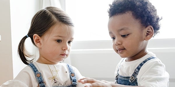 Two children in overalls facing one another playing a game on a tabletop