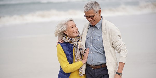 Older couple smiling and walking on the beach