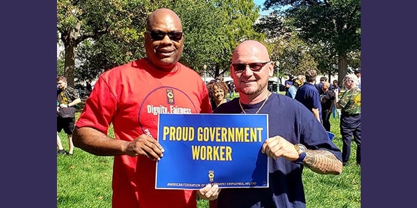 Two AFGE members holding sign that reads proud government worker