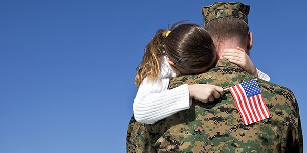 Man in military uniform holding child with an American flag