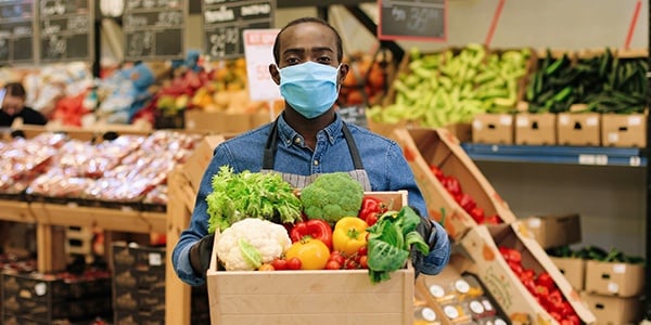 Worker holding a box of produce at a grocery store.