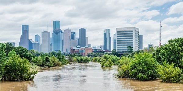 High and fast water rising in Bayou River with downtown Houston in background under cloud blue sky.