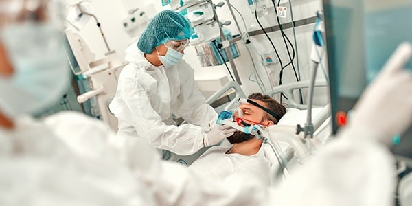 Health care workers in PPE caring for a patient in a hospital bed.