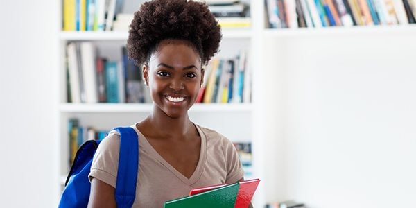 Black woman smiling at camera holding books and a bookbag