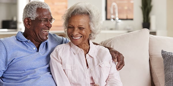 Older Black couple smiling together sitting on a couch.