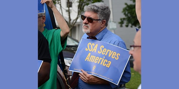 Rally attendee holding signs that reads SSA Serves America