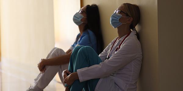 Two medical workers sitting on floor leaning their heads against a wall